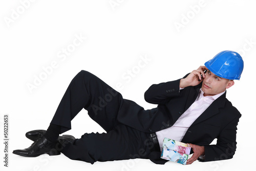 Photo: Architect laying with house made from money Architect laying with house made from money