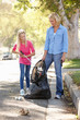 Mother And Daughter Picking Up Litter In Suburban Street