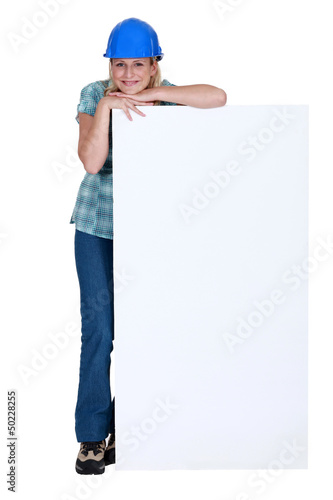 Photo: Woman with protective helmet leaning on a white sign Woman with protective helmet leaning on a white sign