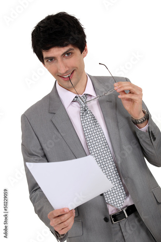 Photo: Businessman holding hiss glasses and sheet of paper Businessman holding hiss glasses and sheet of paper