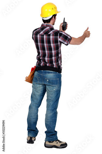 Photo: worker looking at his walkie talkie and making a thumbs up sign worker looking at his walkie talkie and making a thumbs up sign