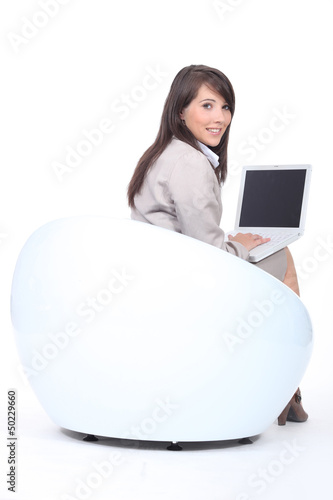 Photo: Young woman in a funky white chair, using a laptop computer Young woman in a funky white chair, using a laptop computer