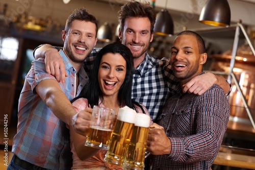Photo: Group of happy friends clinking with beer in pub Group of happy friends clinking with beer in pub