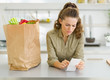 Concerned housewife checking bill after shopping in kitchen