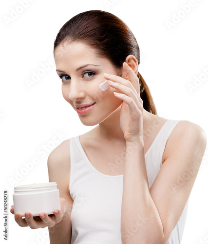 Photo: Woman putting on cream from container on face, isolated Woman putting on cream from container on face, isolated