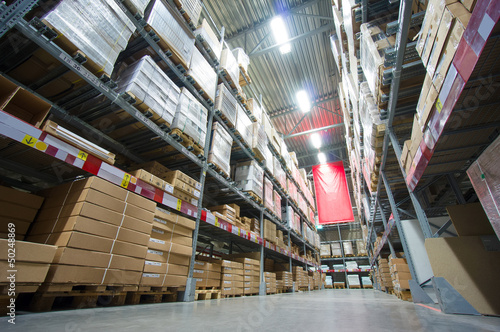 Photo: Rows of shelves with boxes and other goods in modern warehouse Rows of shelves with boxes and other goods in modern warehouse