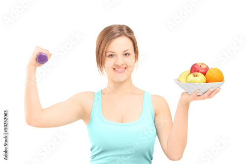 Photo: Beautiful young female posing with a dumbbell and fruits in a bo Beautiful young female posing with a dumbbell and fruits in a bo