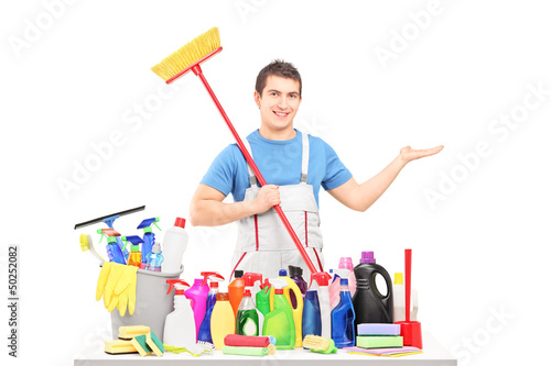Photo: Man in a uniform holding a broom and posing with cleaning suppli Man in a uniform holding a broom and posing with cleaning suppli