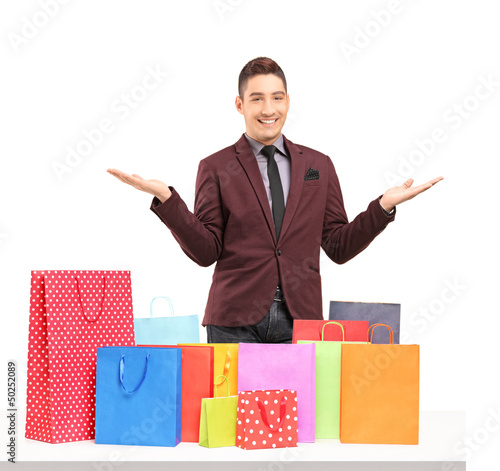 Photo: Satisfied young man posing with plenty of shopping bags on a tab Satisfied young man posing with plenty of shopping bags on a tab