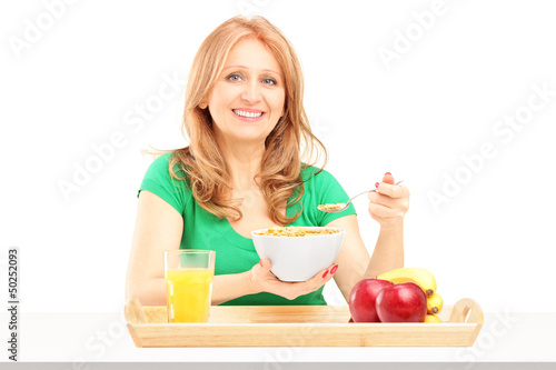 Photo: Smiling woman eating cereals and fruit for breakfast Smiling woman eating cereals and fruit for breakfast