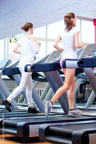 Photo: Two young sporty women run on machine Two young sporty women run on machine