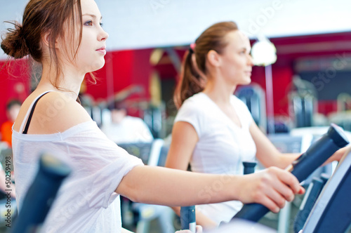 Photo: Two young sporty women run on machine Two young sporty women run on machine