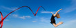 Jymnast with red ribbon jumping against blue sky