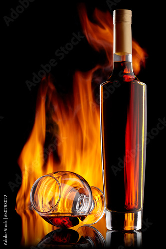 Photo: Bottle and glass of cognac over dark background with flame Bottle and glass of cognac over dark background with flame