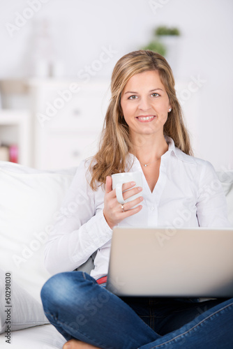 Photo: frau sitzt mit kaffee und laptop auf dem sofa frau sitzt mit kaffee und laptop auf dem sofa