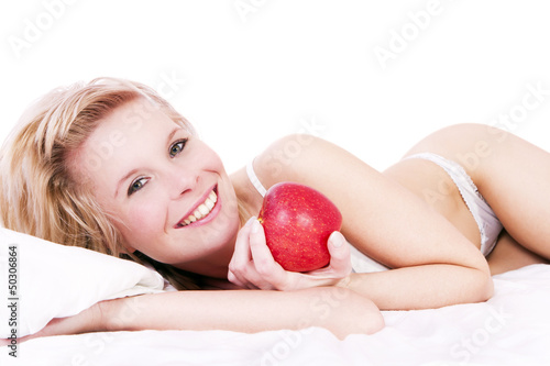 Photo: Beautiful blonde girl lying on the bed, holding apple. Beautiful blonde girl lying on the bed, holding apple.