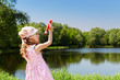 Girl in pink dress and panama from sun stands on bank of pond
