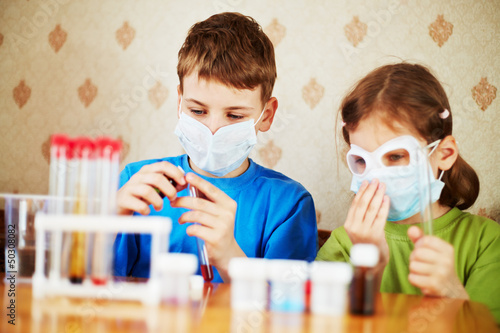 Photo: Boy fills chemical test tube with specimen and girl sits near Boy fills chemical test tube with specimen and girl sits near