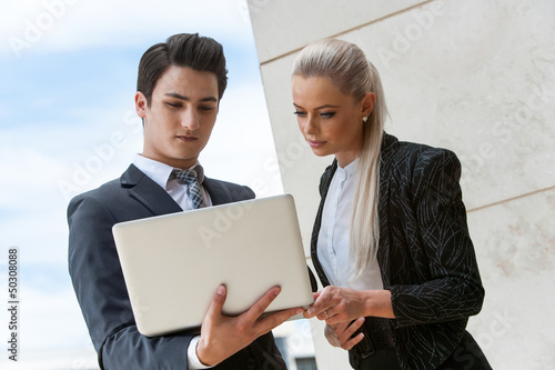 Photo: Young business partners reviewing data on laptop. Young business partners reviewing data on laptop.