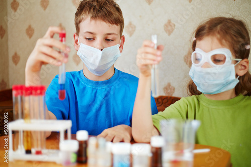 Photo: Boy and girl sit at table with chemical reagents and look Boy and girl sit at table with chemical reagents and look