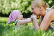 Young smiling mother plays with her baby on grass