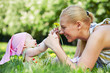 Young smiling mother plays with her baby on grass in spring park