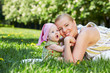 Young mother and her baby snuggle their cheeks, sitting on grass