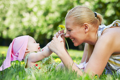 Photo: Young smiling mother plays with her baby on grass in spring park Young smiling mother plays with her baby on grass in spring park
