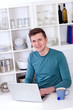 Photo: young man sitting with a laptop and tea cup in the kitchen young man sitting with a laptop and tea cup in the kitchen