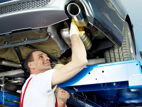 Photo: Two car mechanics fixing the exhaust system of a car Two car mechanics fixing the exhaust system of a car