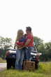 A couple standing in front of a sports car with a picnic basket