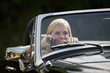 A young woman driving a black sports car holding a mobile phone