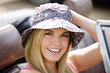 A young woman sitting in a sports car wearing a summer hat