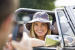 A man photographing a woman in a black sports car