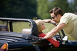A young man speaking to a young woman in a black sports car