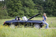 A young woman sitting on a broken down car using a mobile phone