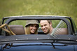 A young couple in a sports car with gardening tools in the back