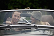 A young couple in a sports car with gardening tools in the back