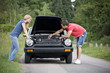 A young couple standing next to their broken down sports car