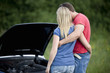 A young couple standing next to their broken down sports car