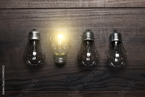 Photo: glowing bulb uniqueness concept on wooden background glowing bulb uniqueness concept on wooden background