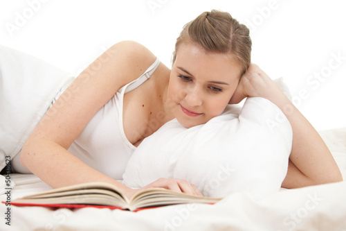 Photo: student woman reading book in white bedding student woman reading book in white bedding