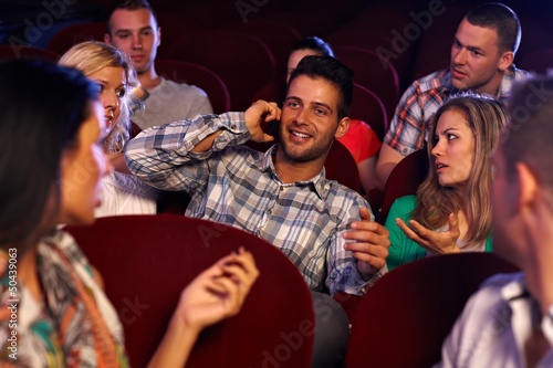 Photo: Confident young man using mobile in cinema Confident young man using mobile in cinema