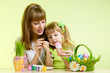 mother and child girl paint easter eggs over green background