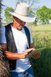 Cowboy leans on hay with tablet computer