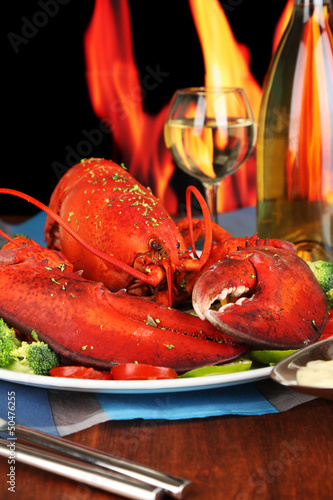 Photo: Red lobster on platter on wooden table on fire background Red lobster on platter on wooden table on fire background