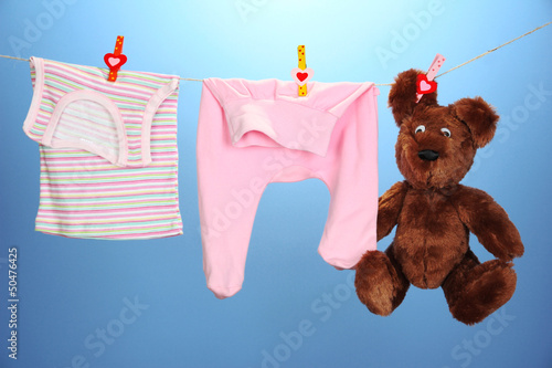 Photo: Baby clothes hanging on clothesline, on color background Baby clothes hanging on clothesline, on color background
