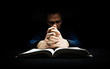 Man praying to God with his hands resting on a bible.