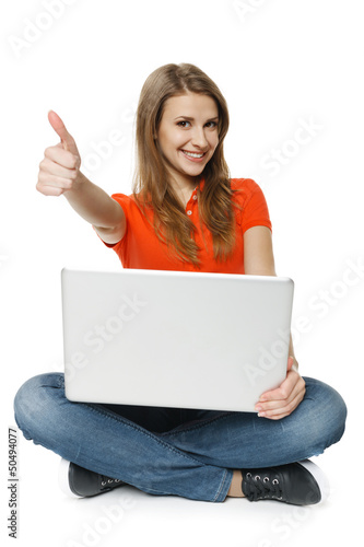 Photo: Young woman sitting on floor with her laptop making thumb up Young woman sitting on floor with her laptop making thumb up