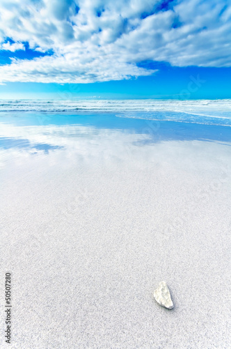 Photo: White rock in a white beach under blue and cloudy sky White rock in a white beach under blue and cloudy sky